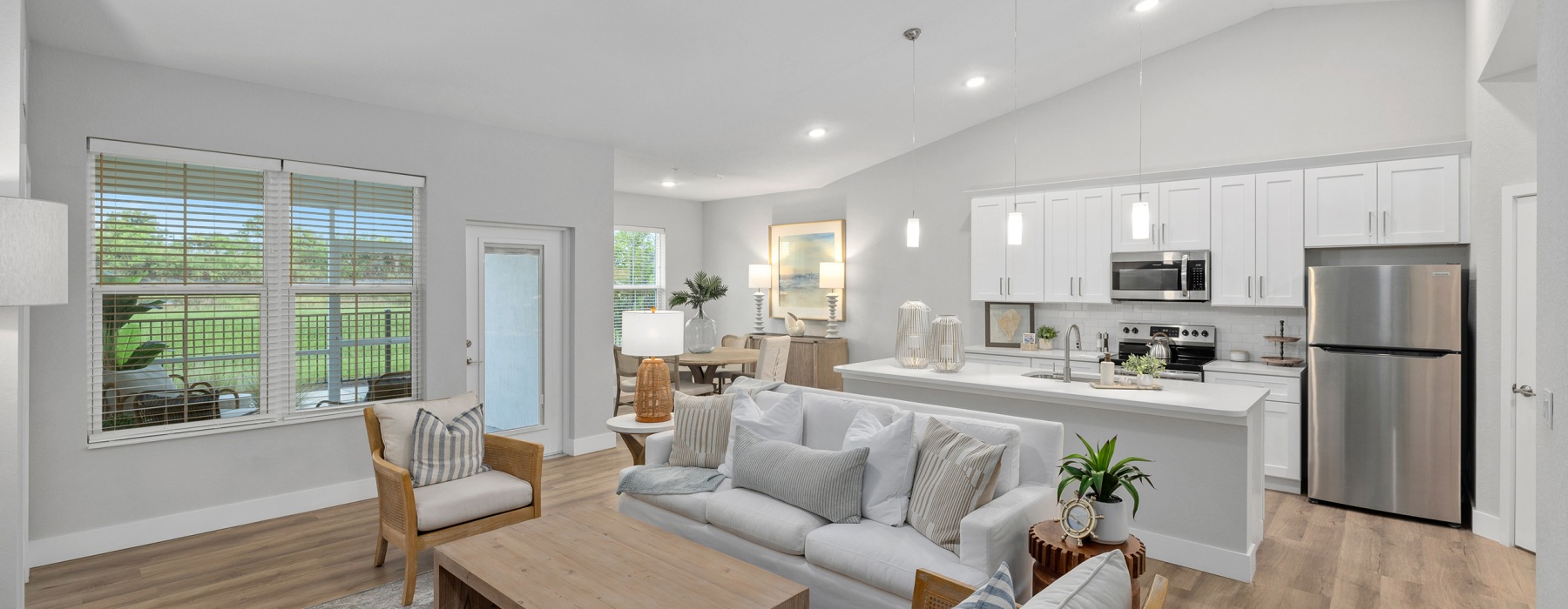 Model living room and kitchen at Encore at Tradition 55+ community in Port St Lucie, FL, featuring wood grain flooring.